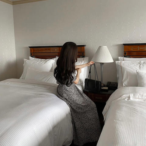 nairoのレトロフラワーワンピースを着てベッドに腰掛ける女性
